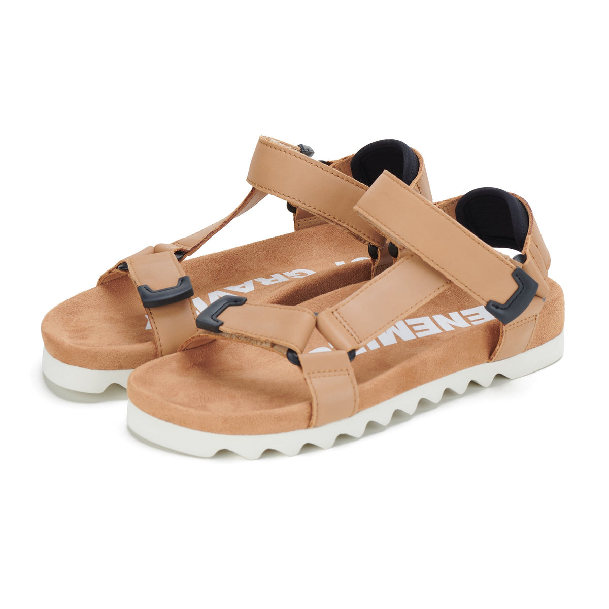 Pair of tan leather strap sandals on white toothed wedge soles, angled view